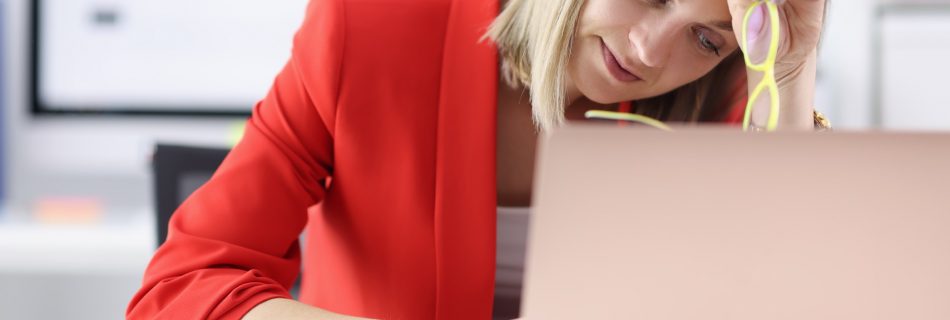 Femme fatiguée assise sur un ordinateur portable avec des lunettes dans les mains