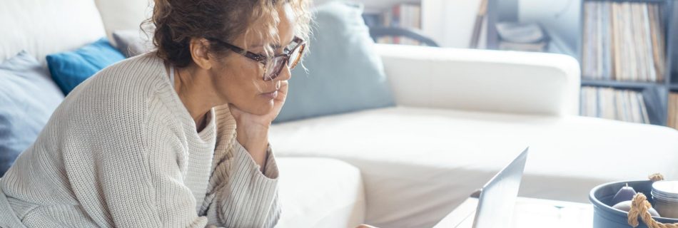Vue latérale d'une femme seule à la maison navigant sur les pages Web d'Internet en utilisant un ordinateur portable assis sur le canapé Les femmes modernes travaillant sur l'ordinateur dans le travail à distance lieu de travail de bureau alternatif Site Web d'adhésion