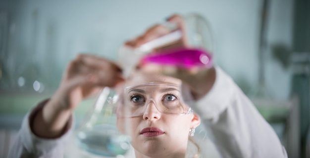 Laboratoire de chimie jeune femme blonde sur le point de verser un liquide rose dans la femme bleue au point