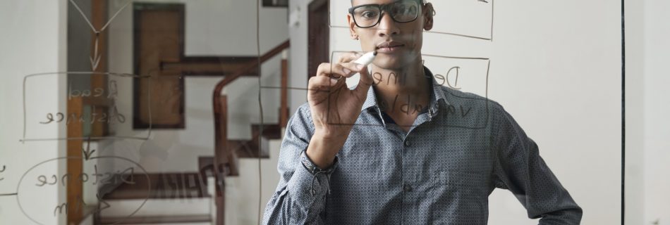 Jeune développeur de logiciels sérieux dessinant un organigramme général sur un mur de verre au bureau de sa société