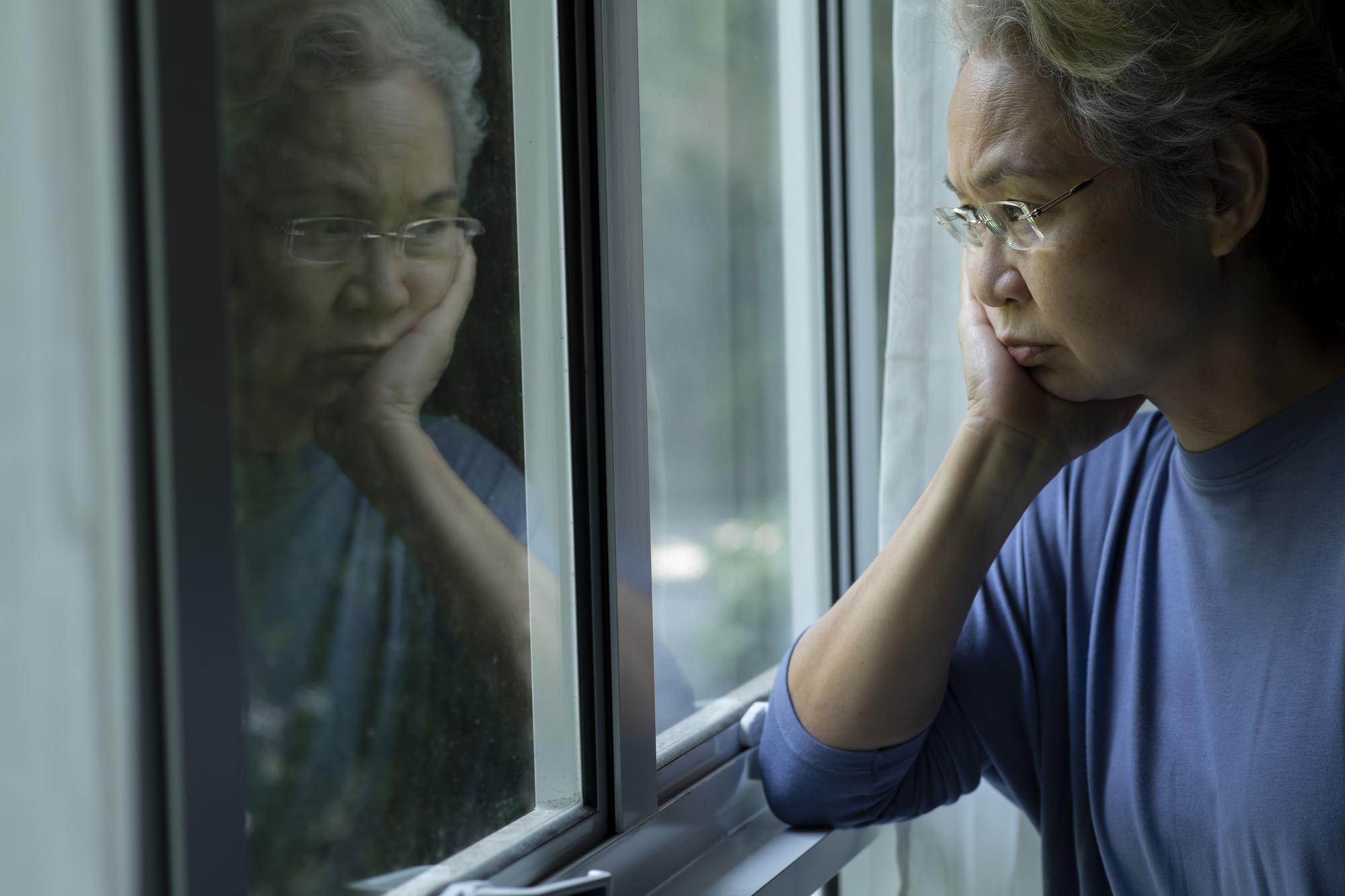 Portrait d'une femme senior asiatique triste et inquiète regardant par la fenêtre à la maison