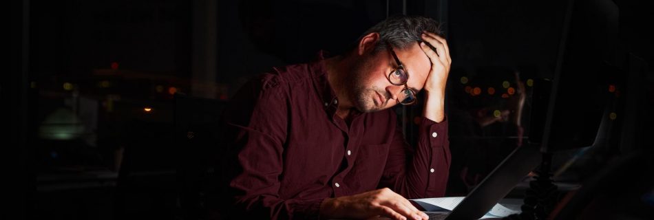 Homme d'affaires fatigué et inquiet sur son lieu de travail au bureau tenant sa tête sur ses mains après avoir travaillé tard dans la nuit sur son ordinateur portable