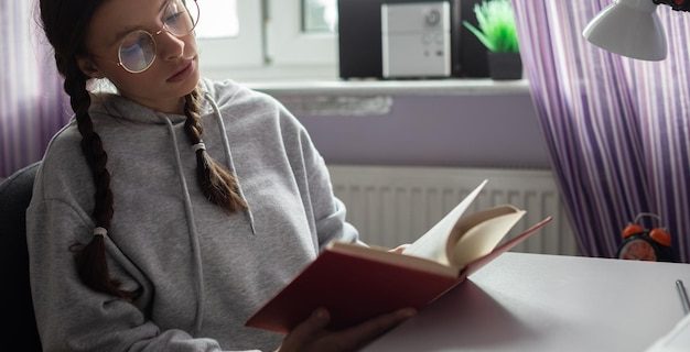 Un étudiant avec des tresses et des lunettes à la maison lit un livre