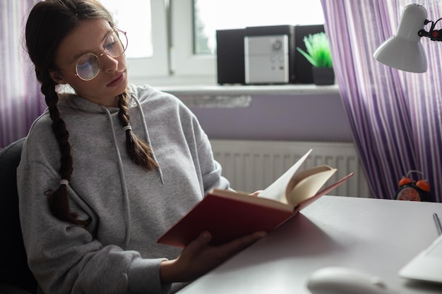 Un étudiant avec des tresses et des lunettes à la maison lit un livre