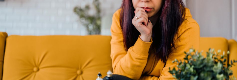 Jeune femme assise sur un canapé jaune et jouant aux échecs dans la chambre